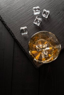 Koyu ahşap masadaki viski ve buz kalıplarının üst görüntüsü.