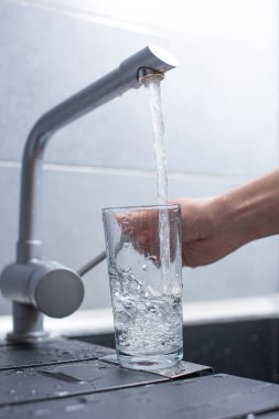 Kadın mutfaktaki musluktan su döküyor.