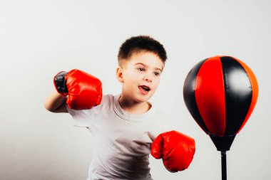 Boks eldivenli ciddi bir çocuk gri arka planda antrenman ve boks yapıyor.
