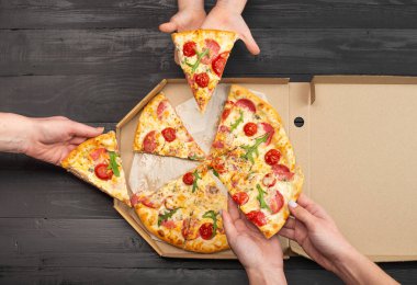İnsanların ellerinde domatesli, salamlı ve peynirli pizza dilimleriyle ahşap masaya oturdukları sahneler. 