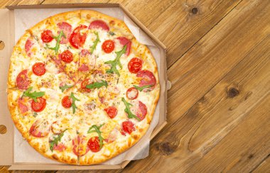 Domatesli, salamlı, peynirli, ahşap masada nefis pizzanın üst görüntüsü. 