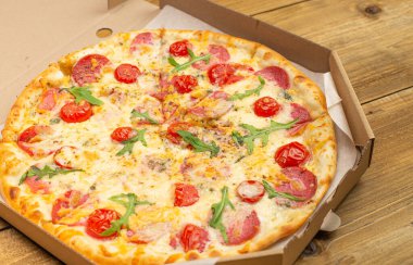 Domatesli, salamlı ve peynirli lezzetli pizzanın ahşap masadaki kutuda yakın plan görüntüsü. 