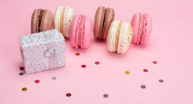 Tatlı, lezzetli badem kurabiyeleri, renkli konfeti ve pembe arka planda hediye kutusu.