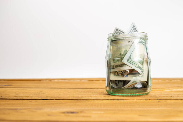 Крупный план стеклянной банки с долларовыми банкнотами на деревянном столе
