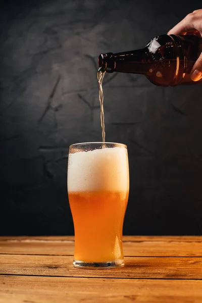 cropped shot of person pouring beer from bottle into glass