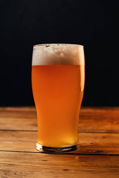 close-up view of cold beer in glass on wooden table on black background 