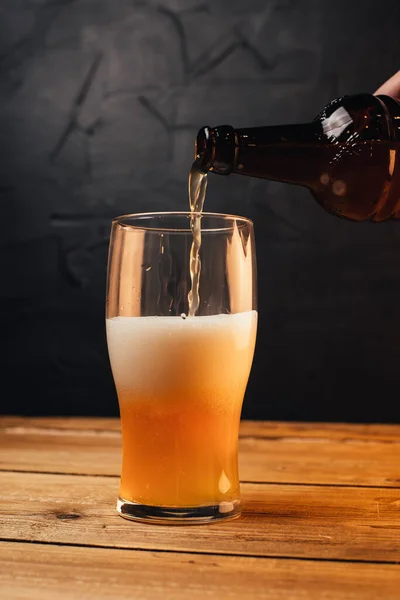 partial view of person pouring beer from bottle into mug on wooden table