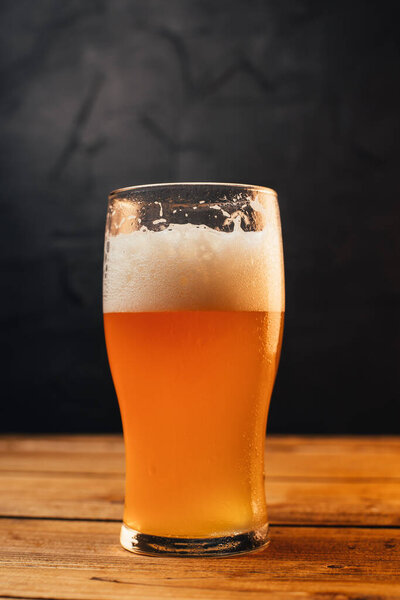 close-up view of cold beer in glass on wooden table on black background 