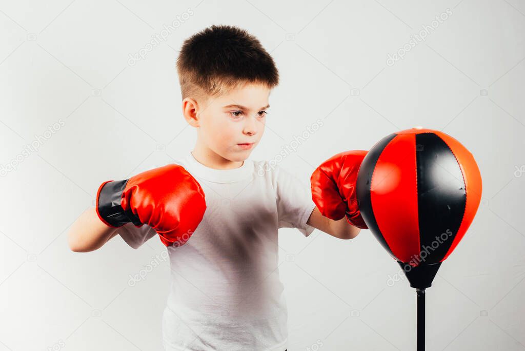 serious boy in boxing gloves training on grey background