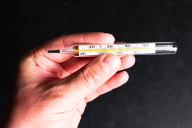 Siyah bir arkaplanda termometreyi tutan el. 