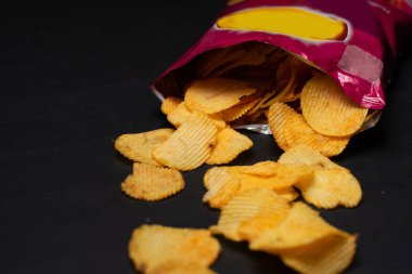 Lezzetli patates cipslerinin yakın plan görüntüsü ve siyah arka plandaki paket.