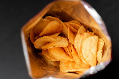Siyah arka planda lezzetli patates cipslerinin yakın plan görüntüsü, seçici odaklanma