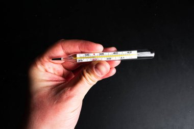 Siyah bir arkaplanda termometreyi tutan el. 