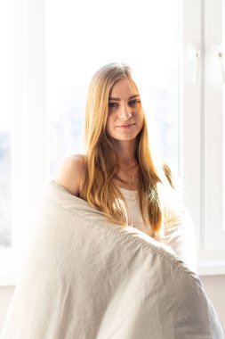 çekici genç bir kadın pencerenin yanında duruyor ve sabahları kameraya gülümsüyor.