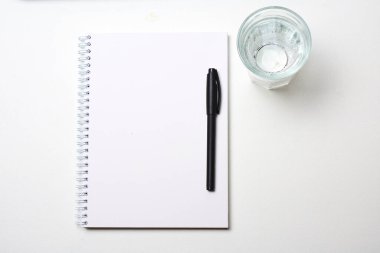 beyaz zemin üzerinde kalem ve bardak su olan defter
