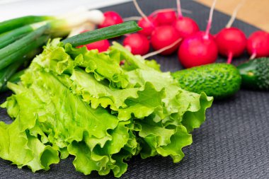 Mutfaktaki masada taze salata yaprakları, turplar ve salatalıklar.