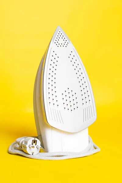 close-up view of modern white iron with plug on yellow background