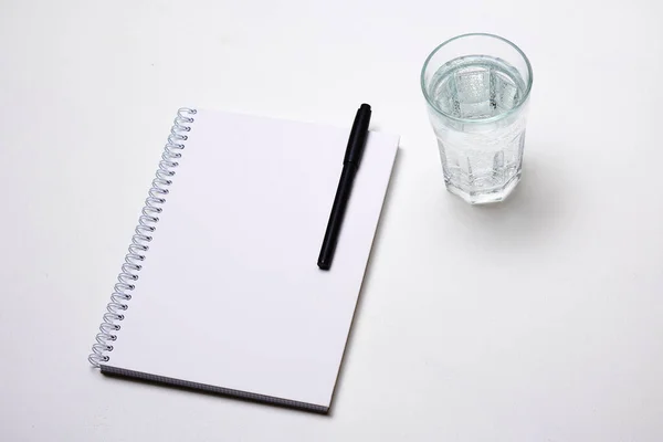 Σημειωματάριο Στυλό Και Ένα Ποτήρι Νερό Λευκό Φόντο — Φωτογραφία Αρχείου