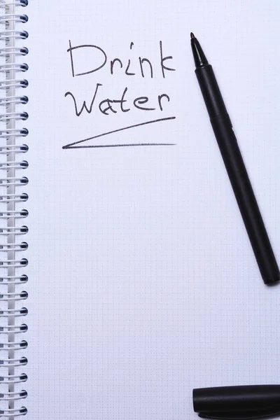 drink water handwriting text written on notebook page and black pen