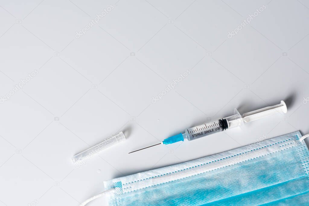 top view of medical mask and syringe on grey background  