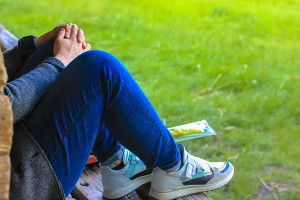 A person sitting on the grass in summertime: hands on knees, blue jeans and white sneakers. — Stock Photo, Image