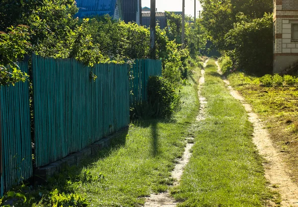 Country road early in the morning: the sun rises above the ground and lights up the grass and houses.