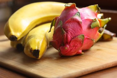 Muz ve pitaias, ejderha meyvesi: olgun, sulu meyveler bir masa üzerinde ahşap bir tahta üzerinde uzanır.