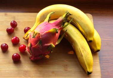 Muz, kiraz ve pitaias, ejderha meyvesi: olgunlaşmış, sulu meyveler bir masa üzerinde bir ahşap tahta üzerinde uzanır.