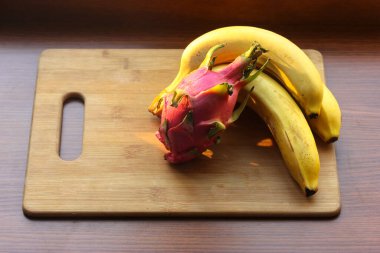 Muz ve pitaias, ejderha meyvesi: olgun, sulu meyveler bir masa üzerinde ahşap bir tahta üzerinde uzanır.