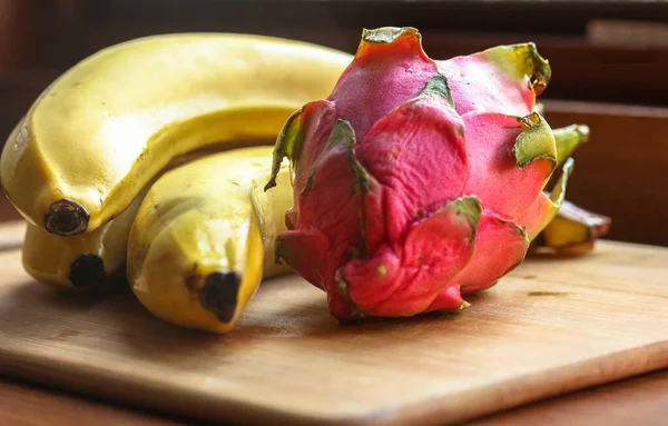 Bananer och pitaias, drakfrukt: mogna, saftiga frukter ligger på en träskiva på ett bord. — Stockfoto