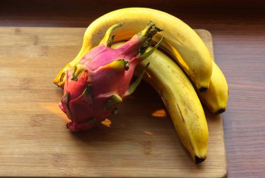 Muz ve pitaias, ejderha meyvesi: olgun, sulu meyveler bir masa üzerinde ahşap bir tahta üzerinde uzanır.