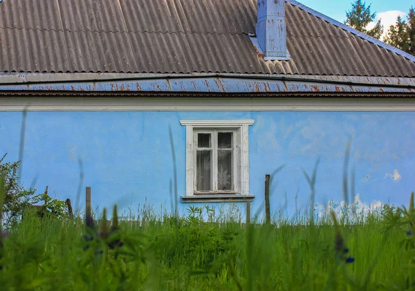 Starý jednopodlažní modrý dům s bílými okny na Ukrajině, vysoká zelená tráva v zahradě před budovou — Stock fotografie