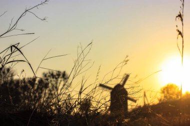 Gün batımında siluet değirmeni ve ön planda çimenler