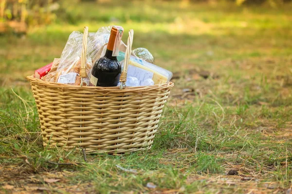 秋の公園で緑の空のグレード上の食品やワインのボトルと木製の茶色のウィッカーバスケット — ストック写真