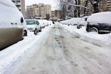 Kışın kar, buz ve park etmiş arabalarla kaplı kaygan bir yol.