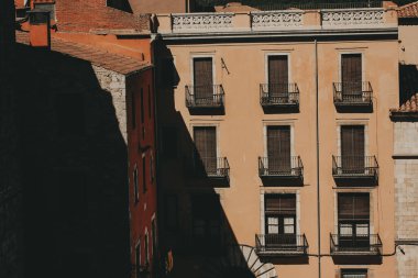 Girona, İspanya, 1 Mayıs 2024. Sıcak güneş ışığında tarihi yapılar inşa etmek. Binanın dış tarafında balkonlar, panjurlu pencereler ve çarpıcı bir kontrastlık yaratan ışık ve gölge etkileşimi.