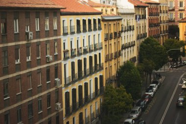 Madrid, İspanya, 2 Haziran 2025 apartman binaları ve sokak havası manzaralı. Arabalar yan tarafa park edilmiş ve ağaçlar yeşillik ekliyor. Şehir manzarası. Bakış açısına göre tarihsel renkli evler.
