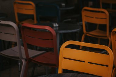 Renkli sarı, kafede kırmızı sandalyeler. Masaların etrafına dizilmiş renkli sandalyelerin yakın plan çekimi canlı ve davetkar bir atmosfer yaratıyor. Boş oturulan açık kafe ayarları. Şehir sokağı