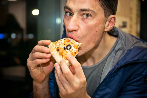 stock image The man eating pizza. Its in the cafe. Holding a piece of pizza in hand, close-up.