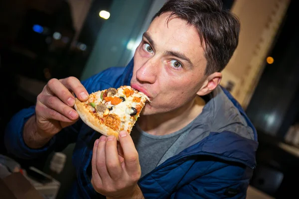 The man eating pizza. Its in the cafe. Holding a piece of pizza in hand, close-up.