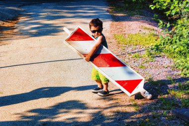 Little boy is carrying a construction site barrier across the street. To overcome difficulties clipart