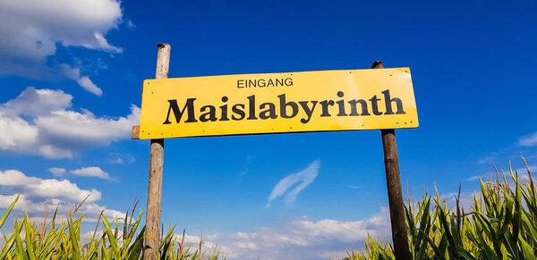 Corn Maze is a maze cut from a corn field. Maize labyrinths are popular with tourists and children. Entrance sign in front of blue sky with lettering in german - entrance Maislabyrinth