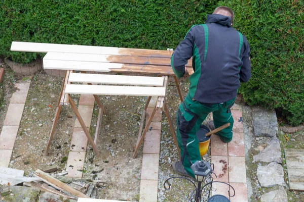 El hombre acaricia pintura protectora en muebles de jardín de madera . — Foto de Stock