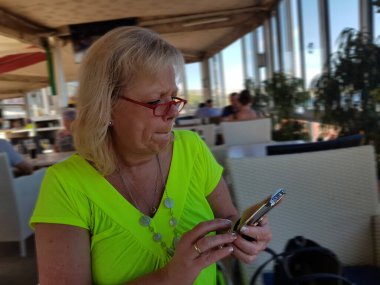 Restoran terasında akıllı telefonuyla mesajlaşan bir kadın. Odaklanmamış bir geçmişi var.