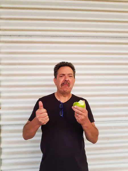 Portrait of a man in front of light background is eating a green sour apple and grimacing.