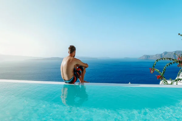 Santorini Greece Oia, young men in swim short relaxing in the pool looking out over the caldera of Santorini Island greece, infinity pool Greece