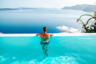 Santorini Yunanistan Oia, havuzda kısa süre yüzen gençler Santorini Adası 'nın Yunan kalderasına, Yunanistan' ın sonsuz havuzuna bakıyorlar.