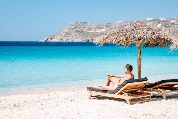 young guy in swim short at the beach of Mykonos Greece, guy at beach chair on the Mykonos beach