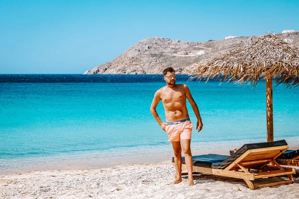 Mykonos Yunanistan plajında kısa yüzen genç adam, Mykonos plajında plaj sandalyesinde oturan adam. — Stok fotoğraf