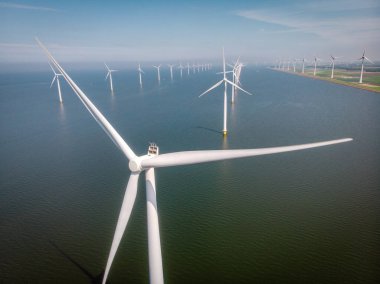 Yel değirmeni parkı Batı Hollanda, okyanusta mavi gökyüzü olan rüzgar türbini, yeşil enerji, küresel ısınma kavramı